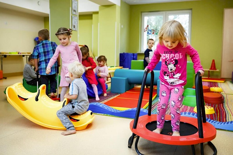 Obraz przedstawia dzieci bawiące się w sali przedszkolnej