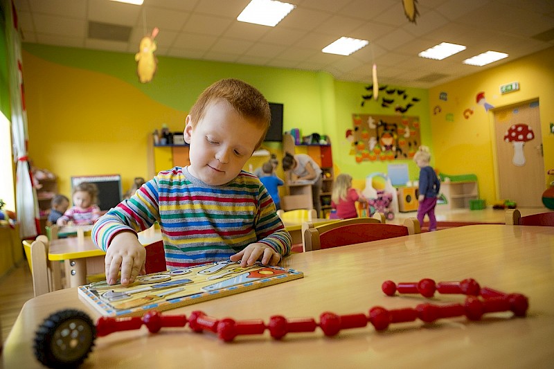 Obraz przedstawia dziecko bawiące się zabawkami w sali przedszkolnej