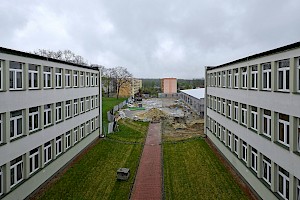 Widok po obu stronach budynków Zespołu Szkół z zewnątrz, w oddali budowa łącznika i okoliczne budynki, drzewa